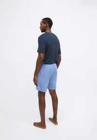 Camisa texturizada azul-marinho de manga curta combinada com calções azul-claro, com cintura elástica. O modelo está descalço.