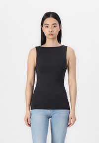 Schwarzes ärmelloses Oberteil mit Bootsausschnitt, aus glattem Material, figurbetonter Schnitt, kombiniert mit hellblauen Jeans.