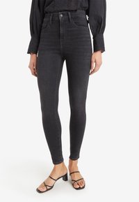 Jeans skinny de talle alto en denim gris oscuro con una textura suave. Presentan un diseño clásico de cinco bolsillos y sutiles detalles de costura.