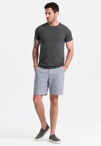 Czarnoszary t-shirt z krótkim rękawem, jasnoszare szorty i szare buty typu slip-on. Osoba stoi pewnie, z rękami w kieszeniach.