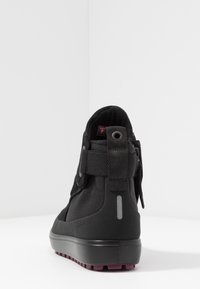 Baskets montantes noires en tissu texturé, avec une languette arrière, une bande réfléchissante et une semelle de traction bordeaux sur fond blanc.