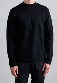 Svart långärmad skjorta i mjukt tyg, med rund halsringning och figursydda ärmar. Kombinerad med mörka texturerade byxor.