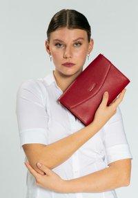 Clutch rossa testurizzata con una pattina curva, chiusura con zip e logo marchiato. Posizionata su uno sfondo chiaro, che mette in evidenza una finitura liscia.