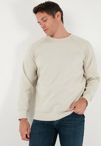 Sudadera beige claro con mangas largas y cuello redondo. Presenta puños y dobladillo acanalados, confeccionada en una tela suave y con textura.