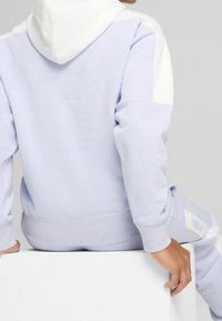 Lichtpaarse hoodie met witte accenten, zachte stof, losse pasvorm en geribbelde manchetten. Gestyled met bijpassende broek met subtiele branding.