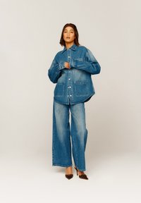 Jeansjakke og vide jeans i mellomblått, med store lommer, knappeåpning og avslappet passform. Glatt tekstur med minimal fading.