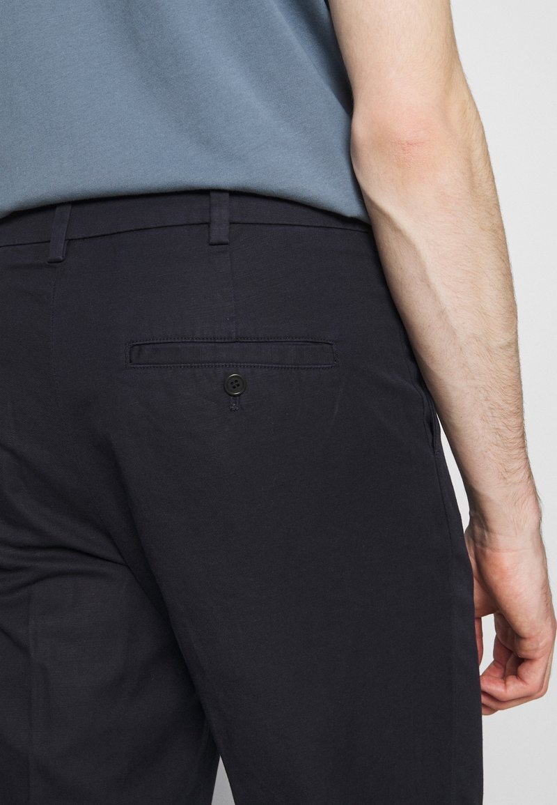 Pantalons bleu marine en tissu lisse, dotés d'une poche arrière à bouton et d'une coupe ajustée, associés à une chemise à manches courtes bleue.