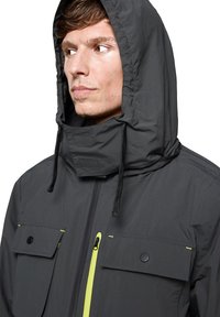 Męska ciemnoszara kurtka z kapturem, z przednim zamkiem błyskawicznym, dwoma dużymi kieszeniami na piersi i żółtymi akcentami na zamkach; wykonana z lekkiego, wodoodpornego materiału.