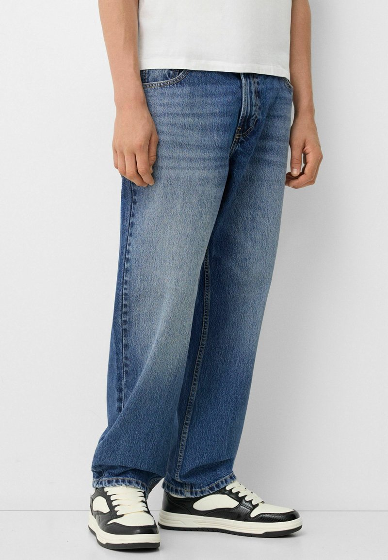 Jean taille large bleu clair en denim, avec un effet délavé, un design classique à cinq poches et une fermeture à bouton à l'avant.