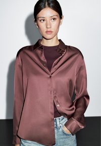 Maroon satin shirt with a smooth texture, button-down design, and long sleeves, paired with light blue jeans.