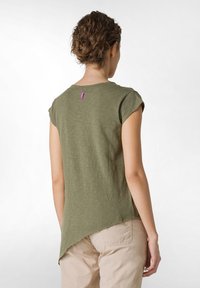 Bluză verde măslinie cu mâneci scurte, având un tiv curbat și o țesătură texturată. Prezintă o etichetă mică violet pe decolteul din spate. Design casual.