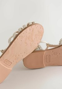 Silver braided sandals with textured soles. Detailed unicorn and star patterns on the beige rubber undersides. Size label visible.