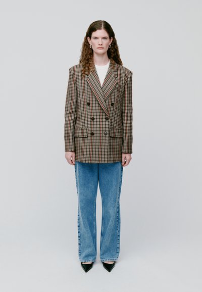 Blazer de cuadro de doble botonadura en tonos marrones y rojos, combinado con unos jeans de denim de pierna ancha en azul claro y unos tacones negros de punta.