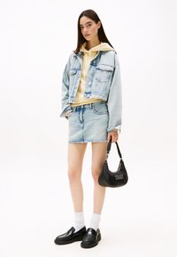Jeansjakke, gul hettegenser, denimskjørt, svarte loafers, hvite sokker, og svart håndbag med logo. Lys og klassisk fargepalett.