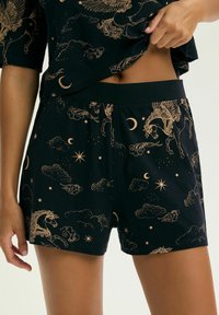 Czarny komplet szortów i topu z złotymi nadrukami o tematyce niebiańskiej, w tym skrzydlate konie, półksiężyce, gwiazdy i chmury, noszony przez osobę.