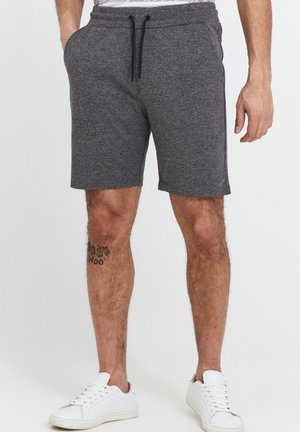 Pantalones cortos atléticos grises hechos de una tela suave, con una cintura ajustable con cordón, bolsillos laterales y un corte relajado. Combinados con zapatillas blancas.