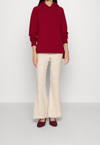 Sudadera con capucha burdeos con bolsillo frontal; combinada con pantalones acampanados crema con patrón texturizado; bailarinas tejidas burdeos.