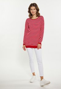Maglione a maniche lunghe a righe rosse e bianche con scollo rotondo e base rossa, abbinato a pantaloni skinny bianchi e scarpe da ginnastica bianche.