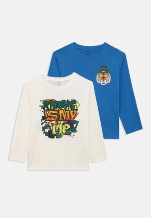 Two long-sleeve kids' shirts: white with colorful "Music is my life" graffiti text, blue with tiger wearing green beanie graphic on chest.
