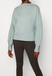 Helles blaues Sweatshirt mit Rundhalsausschnitt, lockerer Passform und langen Ärmeln. Kombiniert mit dunkelbraunen Leggings für einen kontrastierenden Look.