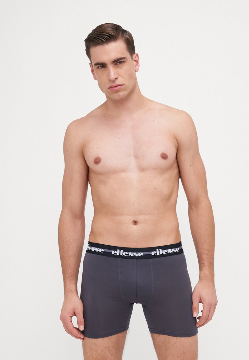 Graue Boxer Shorts mit einem schwarzen elastischen Bund, der mit weißem "ellesse"-Branding versehen ist. Glatte Textur, figurbetonter Schnitt und Oberschenkellänge.