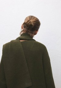 Maglione verde scuro lavorato a maglia con trama a coste, caratterizzato da un design avvolgente e ampio colletto, drappeggiato sulle spalle.