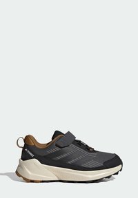Baskets de sport noires avec semelles en caoutchouc, tige en mesh et accent marron au niveau du talon. Dispose d'une sangle Velcro et d'un design texturé.