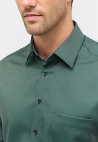 Groene button-up shirt met een gestructureerde stof, voorzien van een puntige kraag, borstzak en donkere knopen. Verfraaid met een gemusterde binnenkraag.