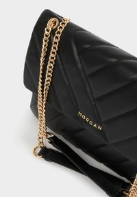 Borsa a tracolla nera trapuntata con una catena dorata. Presenta una texture liscia, un marchio dorato e una forma strutturata.