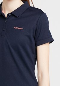 Mörkblå polo skjorta i bomullsblandning, med klassisk krage, korta ärmar och en rosa logotyp på bröstet.