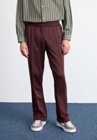 Maroon sweatpants with an elastic waistband, straight cut, and side stripes; worn with a vertically striped green and white shirt.