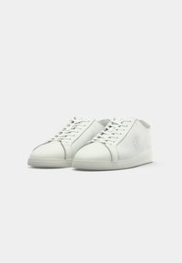 Pair of white leather low-top sneakers with laces, subtle logo on side, and textured finish, displayed on a white background.