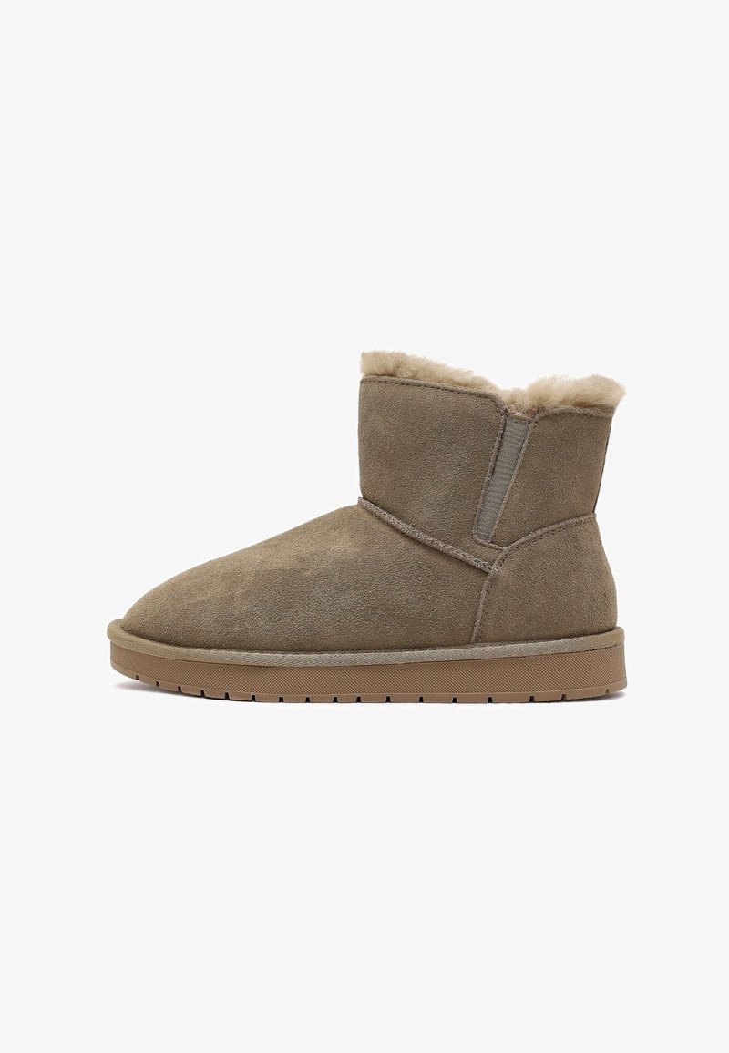 Bottines en suède marron avec une doublure douce en fausse fourrure, bout rond et semelle en caoutchouc plate. Elles sont dotées de panneaux latéraux élastiques.