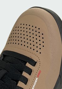 Ruskeat urheilulliset kengät, joissa on rei'itetty päällinen, mustat nauhat ja kontrastoiva kumipohja. Varustettu tekstuuripinnalla ja hienovaraisella brändäys-yksityiskohdalla.