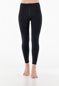 Leggings noirs taille haute en matière extensible, dotés d'une fermeture éclair à l'avant et d'une texture lisse, ajustés de la taille à la cheville.