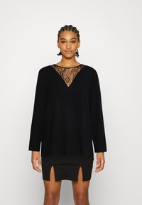 Top preto de mangas compridas com um decote em V de renda, combinado com uma saia preta mini com duas fendas frontais. Textura de tecido suave.