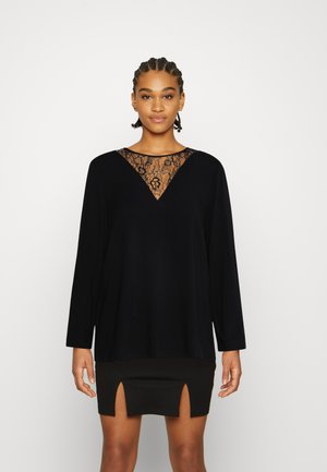Top preto de mangas compridas com um decote em V de renda, combinado com uma saia preta mini com duas fendas frontais. Textura de tecido suave.