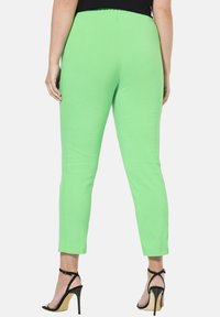 Pantalons verts, extensibles et ajustés avec une taille élastique, associés à des sandales à talons hauts noires. Présentent une texture lisse et une coupe à longueur de cheville.