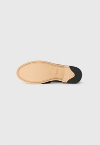 Leather shoe sole in beige with a textured surface, black accents, and contrasting stitching. Features a smooth finish and rounded shape.