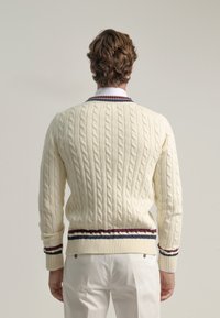 Suéter de punto trenzado crema con dobladillo a rayas burdeos y azul marino acanalado, que presenta un escote redondo y mangas largas. Patrón texturizado en toda la prenda.