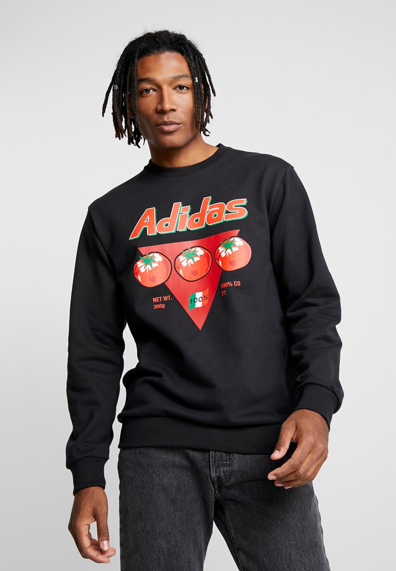 Felpa nera in cotone con girocollo. Presenta una grafica colorata di un pomodoro e il logo "Adidas" in bold verde e rosso.