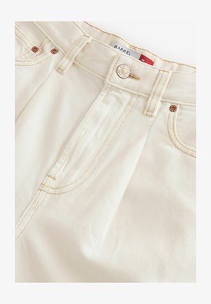 Kreemivärvilised teksapüksid sirge lõikega, millel on vasksed detailid, toon-toonis õmblused ja nähtavad külgseemed, mis annavad struktuuri.