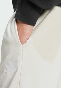 Ljusbeiga sweatpants med en texturerad yta och en svart mudd. Har en sidficka och en diskret grå adidas-logotyp på benet.