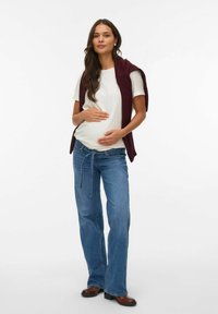 Maternity outfit featuring a fitted white t-shirt, loose-fit blue jeans, and a maroon vest draped over the shoulders. Smooth textures and casual design.