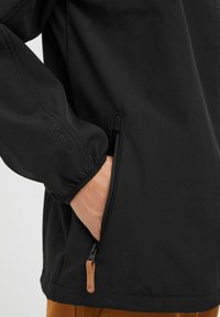 Fekete softshell dzseki cipzáras zsebbel, elasztikus mandzsettákkal és bőr húzótárral. Elegáns, sima textúra és testhezálló dizájn.
