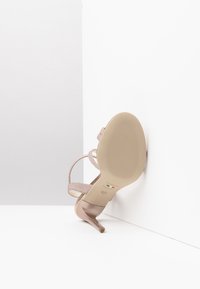 Beige højhælede sandaler med et tekstureret stropdesign, spidse tæer og en glat sål med ribbetræk langs bunden.