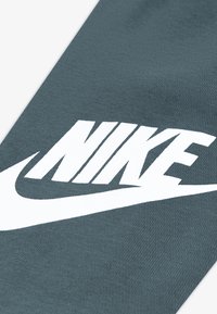 Λογότυπο της Nike τυπωμένο με λευκά γράμματα σε υφασμάτινο, σκούρο πράσινο φόντο με υφή. Ο σχεδιασμός περιλαμβάνει μια έντονη καμπύλη γραμμή και τολμηρή γραμματοσειρά.
