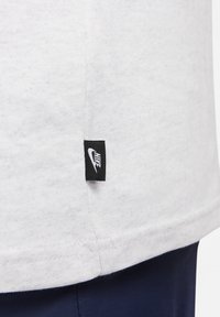 Vit bomull T-shirt med en synlig söm och en liten svart Nikeetikett på sidan, placerad mot marinblått material.