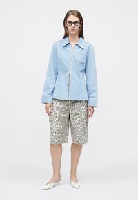 Ανοιχτό μπλε τζιν μπουφάν με φερμουάρ και γιακά με σημείο, συνδυασμένο με γκρι σορτς με λεοπάρ μοτίβο μέχρι το γόνατο. Το μοντέλο φοράει λευκά mules με τακούνι.