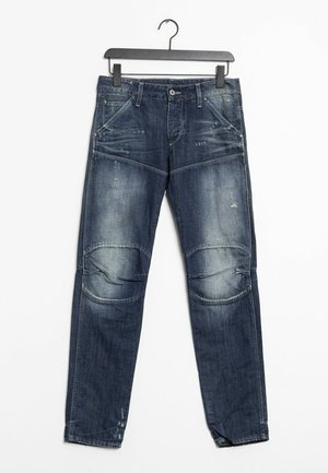 Dunkelblaue Jeans aus Denim mit ausgewaschenen und abgenutzten Details, Knieeinsätzen, Fronttaschen, Gürtelschlaufen und einem Knopfverschluss an einem schwarzen Bügel.